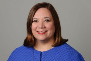 A headshot of Dr. Jennifer Lease Butts, Director of the Honors Program, with a big smile, wearing a royal blue suit jacket against a gray background.