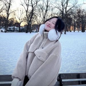 Trang, an Honors Ambassador Coordinator, smiling in a white coat with white ear muffs with snow on the ground and trees in the background