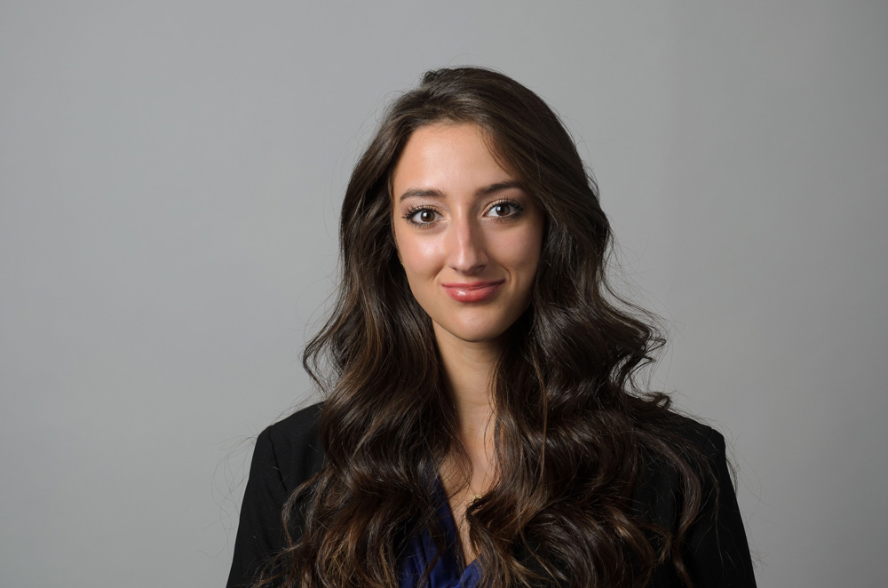 Tess Clark smiling at the camera wearing a black blazer against a gray background