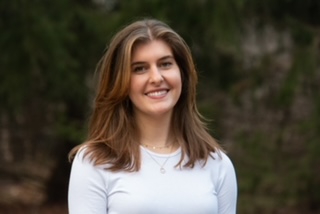 Smiling outdoors, wearing a white shirt.