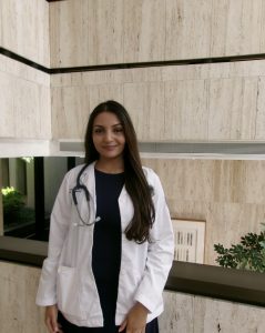 Radha Patel smiling and wearing a white coat and stethoscope